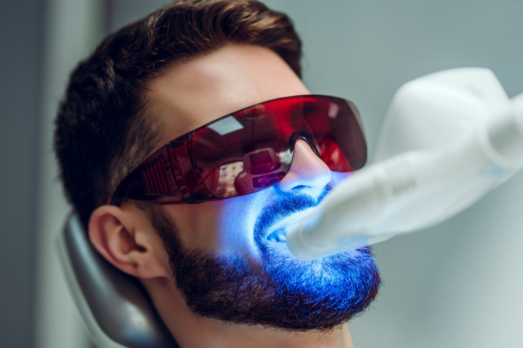 Teeth whitening. Man having teeth whitened by dental UV laser whitening device. Teeth whitening machine,eyes protected with glasses.