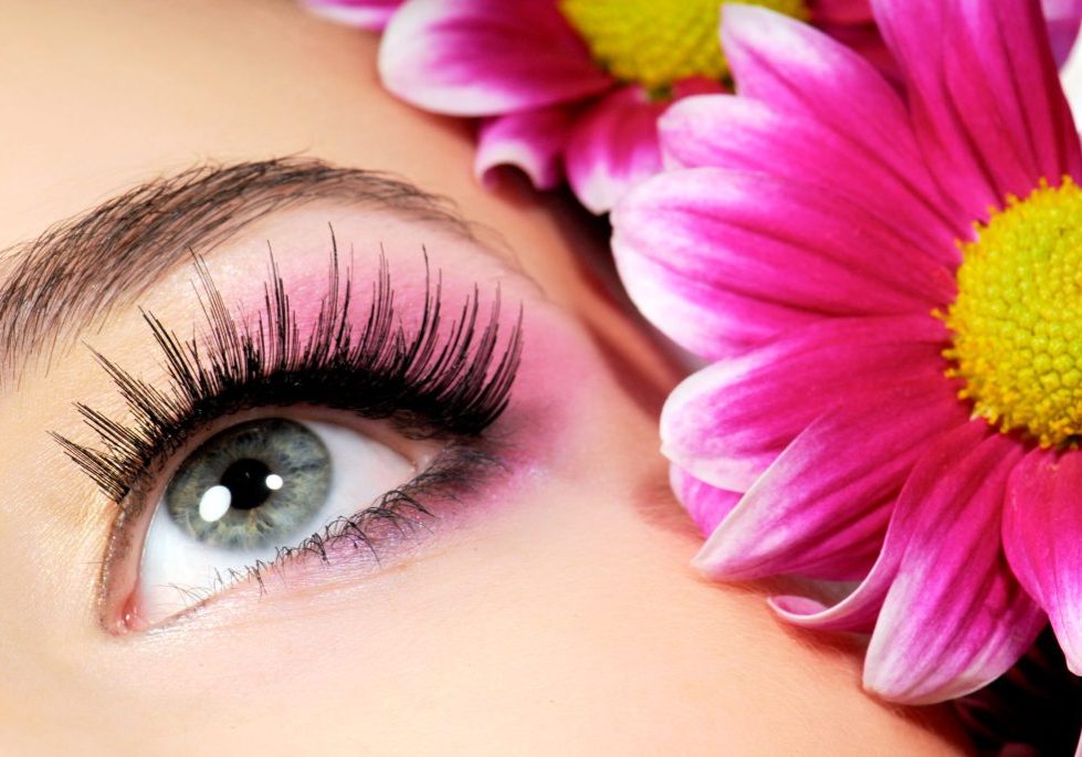 Close-up of woman green eye. Pink flower on background.